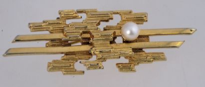 A 1960s to 1970s Brutalist brooch in gold tone metal with a cultured pearl and a rollover clasp.