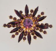 A large 1950s to 1960s amethyst colour rhinestone brooch in a gold tone setting with a roll over
