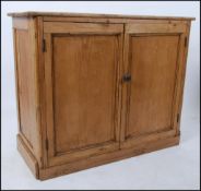 An early 20th century pine school - estate cupboard having plinth base with double doors and shelf