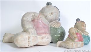 A graduating pair of hand painted carved wooden reclining Buddha children.