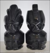 A pair of unusual glass carved inuit figurines. Each with carved warrior head on square bases.