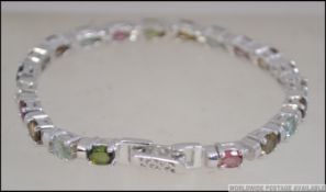 A silver and tourmaline line bracelet, each stone being multicoloured with double clasp.