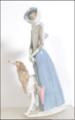 A large Lladro figure of a lady walking a Afgan hound, with impressed stamps to base.