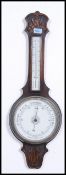 An Edwardian carved oak aneroid wall banjo barometer having an enamelled dial below a mercury