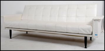 A 1970's G-Plan white faux leather sofa - sofa bed being raised on ebonised dansette legs with