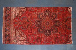 A 20th century handwoven large Persian rug of reduced size with red ground having black medallion