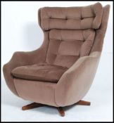 A good 1960's Parker Knoll batwing swivel armchair being raised on a teak quadruped base having