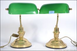 A pair of 20th century bankers desk lamp having a green glass shade being raised on a brass stands