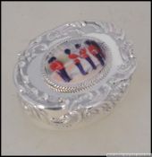A sterling silver embossed pill box having hinged lid inset with enamel pictorial of the Queens