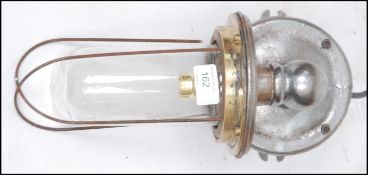 An Industrial cast metal heavy set bulkhead / dairy lamp with caged pendant style bulb on polished