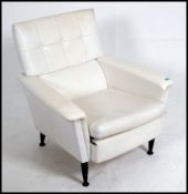 A 1970's G-Plan white faux leather retro armchair being raised on ebonised dansette legs with brass