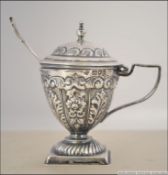 A silver hallmarked mustard pot and spoon in the form of a trophy urn in the rococo style.