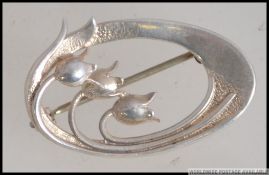 A silver ladies brooch by Ola M Gorie in the Art Nouveau style having 3 tulips with swirl mount,