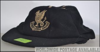 A Vintage early 20th century school cap in black with rope braid having central crest with latin