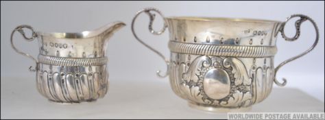 A silver hallmarked Victorian twin handled sugar bowl and creamer cast in relief with rococo scroll