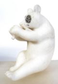 A carved white marble figurine of a panda bear eating bamboo. The bear in seated position.