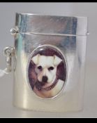 A silver vesta case with enamel image of a dog to the case. Lozenge form with hinged top.