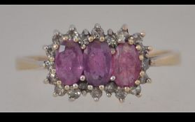 A hallmarked 9ct gold cluster ring set with three oval cut pink sapphire surrounded by a halo of