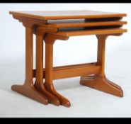 A 1970's retro teak wood nest of tables being raised on shaped legs with stretchers having