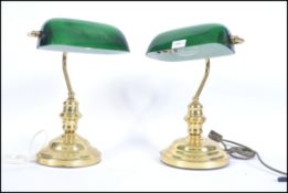 A pair of 20th century bankers desk lamp having a green glass shade being raised on a brass stands