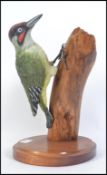 A beautiful hand carved wooden figurine of a woodpecker on a tree stump and raised on a plinth base