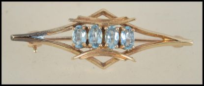 An early 20th century 9ct gold bar brooch set with four oval cut aquamarine stones with lever hoop