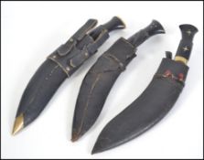 A set of 3 good asiatic Kukri knives having shaped blades with leather scabbards.