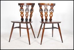 A par of retro Ercol fleur D lys dining chairs having saddle seats and raised on turned legs united