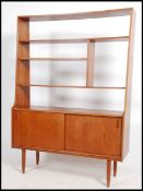 A 1970's Danish teak wood room divider bookcase being raised on tapered legs with tambour cupboard
