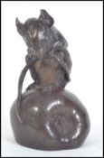 A 20th century bronze figure of a mouse sitting atop of an apple nibbling on it's own tail.