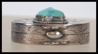 A silver and turquoise set ladies chase decorated oval vignette / pill box with hinged centre.