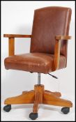 A late 20th century tan leather and oak office swivel chair being raised on castors with swivel