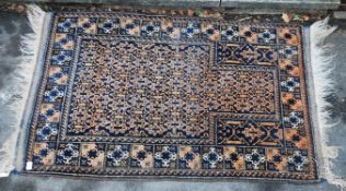 An early 20th century prayer rug with central mihrab on a black and red / blue ground with tassled