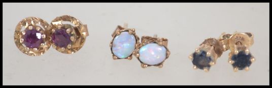 Three pairs of 9ct gold stud earrings individually set with opal, red stone and dark stone.