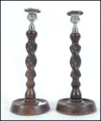 A pair of early 20th century oak barley twist candle sticks raised on circular bases with silver