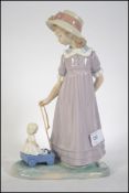A Lladro figurine of a girl trailing a pull along toy cart containing a doll. Stamped to base.