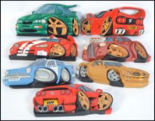A collection of 7 hand carved and painted wooden wall plaques of vehicles to include Ferrari,