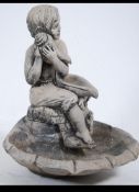 A well weathered reconstituted stone garden water feature of a maiden sat upon an opened clam shell.