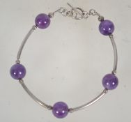 A white metal bracelet with purple ball and tube links an toggle clasp. Measures approx 8 inches.