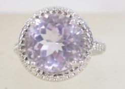 A silver white metal ladies dress ring with large round cut purple stone surrounded by a halo of