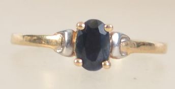 A 9ct gold ring set with an oval cut sapphire with white gold accent shoulders. Tests 9ct gold.