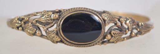 A vintage yellow metal cuff bangle with onyx set cabochon and leaf designed shoulders.