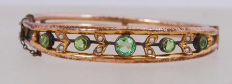 An early 20th century rolled gold bangle set with seed pearl and green faceted stones.