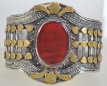 A silver cuff bangle set with a large carnelian cabochon with brass metal and filigree decoration.