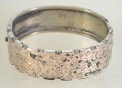 A Victorian silver hinged bangle half engraved with swirling leaf design and castellated edge with