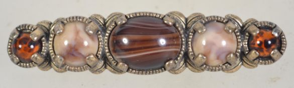 A white metal Miracle brooch set with agate cabochons with toller clip clasp. Measures 6.