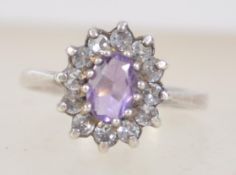 A white metal cluster ring set with central purple stone. Size Q.