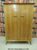 A retro 1960s/70s wardrobe raised on tapering splayed feet, with 'Hamptons, Pall Mall,