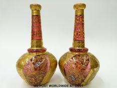 A pair of cranberry glass bottle vases with gilt and enamel decoration of flowers amongst foliage,