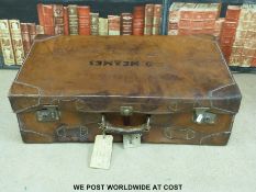 A vintage brown leather suitcase with tickets and shipping labels.